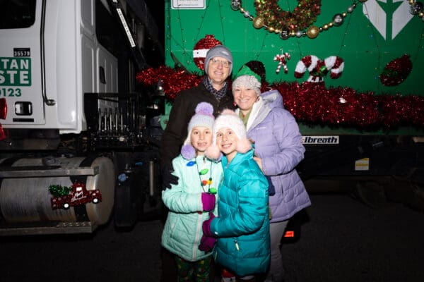 Spartan Waste employee posing with their family in front of the decorated Spartan Waste parade truck.