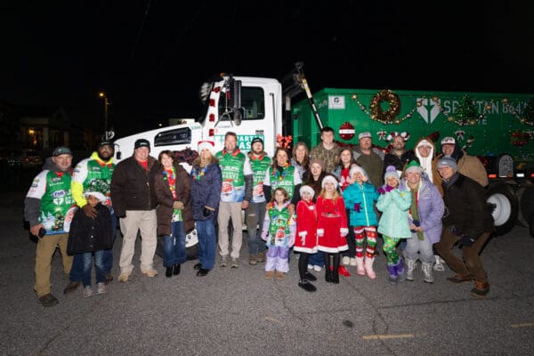 Full Spartan Waste team smiling in front of their Christmas parade truck decorated with holiday lights in downtown Spartanburg.